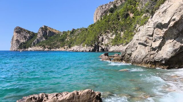 Rough sea waves crashing on rocky shore at Marina del Cantone, Nerano, Sorrento Peninsula, Italy. Historic watchtower on the cliff, turquoise water and sunny summer landscape video footage