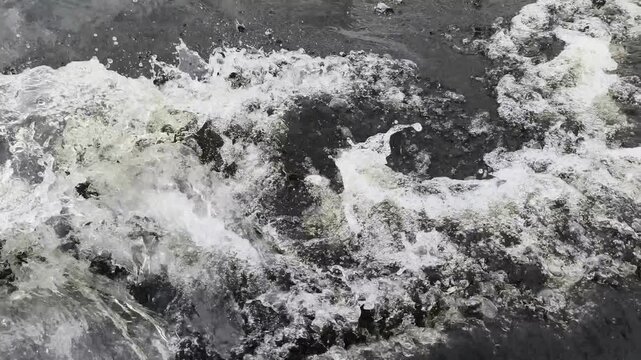 Powerful waves crash and churn in dramatic black and white motion, capturing raw energy of turbulent water as it foams and surges over unseen rocks in a timeless, cinematic display of nature s force
