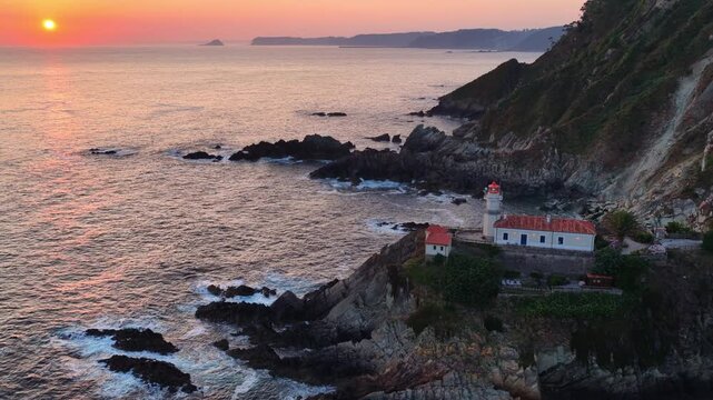 orbiting drone shot of Cudillero lighthouse in Asturias, Atlantic coast of Spain, sunrise in Cudillero, lighthouse on a cliff in the Atlantic Ocean, travel, adventure concept
