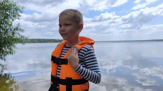 A toddler in a bright orange life jacket stands by the calm water, highlighting essential child water safety and the peace of mind that proper gear brings to family outings near lakes and rivers.