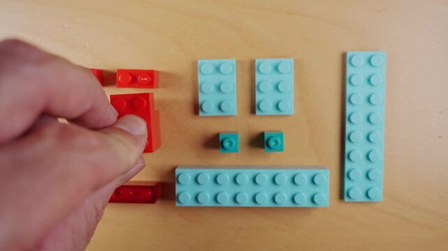 Male hands assembling and disassembling red building blocks on a wooden table, a creative hobby invoking nostalgia and childhood memories of playing with colorful plastic toy collectibles