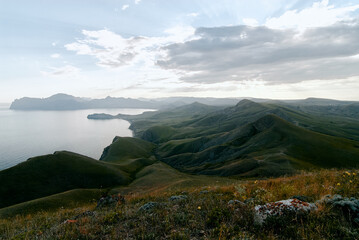 A sweeping coastal landscape of rolling green hills descending to a calm sea beneath a dramatic sky, evoking tranquility, openness and natural beauty for travel, nature, and outdoor themes. © Loginova