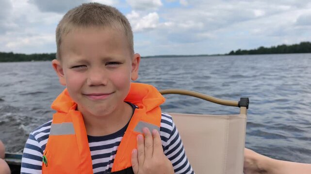 A cheerful child in a bright orange life jacket enjoys a safe boat ride on calm waters, showcasing the importance of water safety gear while capturing the joy and freedom of a sunny day out on lake