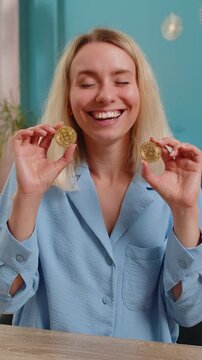 Young blond businesswoman stock trader earning bitcoins after online monitoring trading operations. Increasing wealth financial prosperity. Freelancer woman showing BTC crypto coins at desk in room