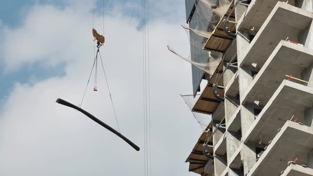 Construction crane lifting structural element alongside a modern building skeleton under development