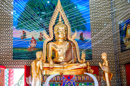 Golden Buddha statue inside a traditional Thai temple surrounded by mural paintings and sacred white ceremonial threads, representing Buddhism, Thai culture, architecture, spirituality, and heritage