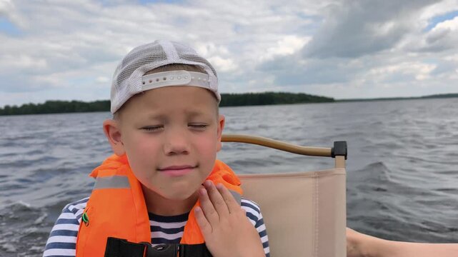 A cheerful child in a bright orange life jacket enjoys a safe boat ride on calm waters, showcasing the importance of water safety gear while capturing the joy and freedom of a sunny day out on lake