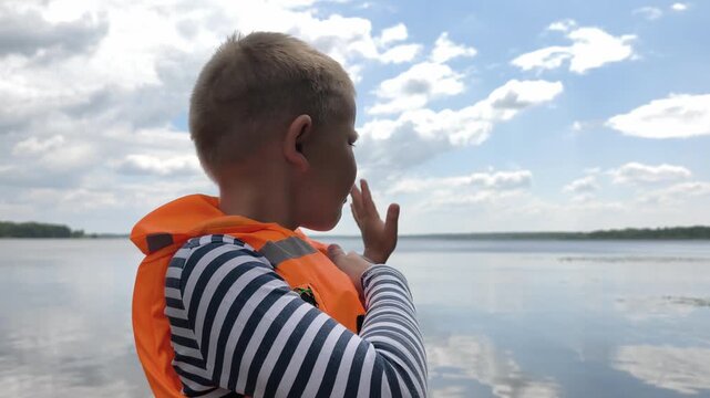 A toddler in a bright orange life jacket stands by the calm water, highlighting essential child water safety and the peace of mind that proper gear brings to family outings near lakes and rivers.