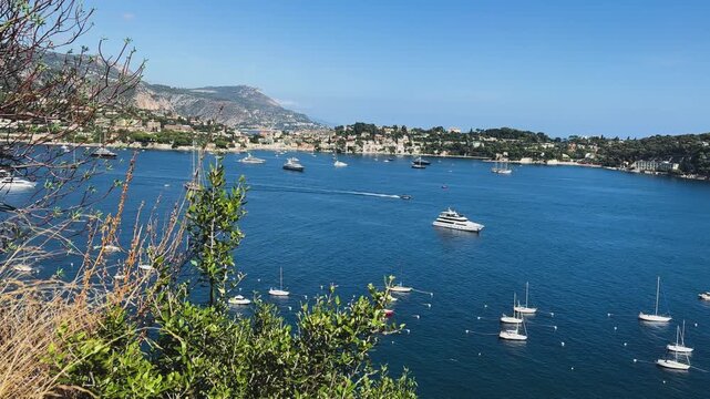 Elevated view of yachts and sailboats across Villefranche-sur-Mer Bay, framed by Mediterranean vegetation and surrounded by scenic coastal hills.