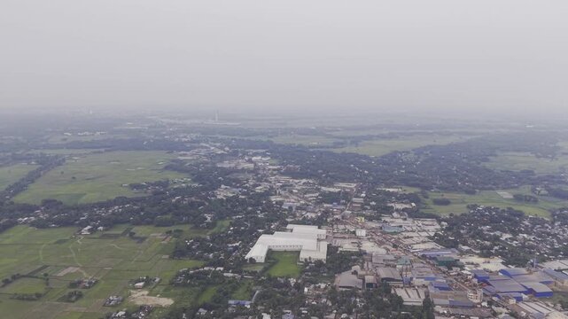 Drone shot with a steady rightward movement over an industrial and residential area in Khajanagar, Kushtia, featuring factories, infrastructure, buildings, and rural surroundings.