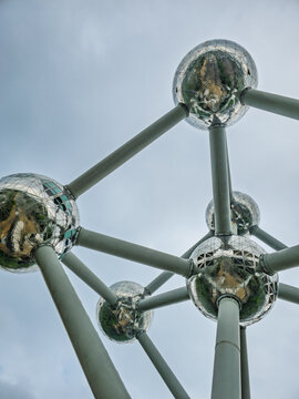 Brussels, Belgium. April 18, 2026, Atomium structure showing spheres connecting by tubes, reflecting surrounding buildings and trees under a cloudy sky