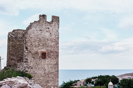 Ancient Stone Castle Ruins Overlooking Calm Sea and Coastal Village Under Pale Sky