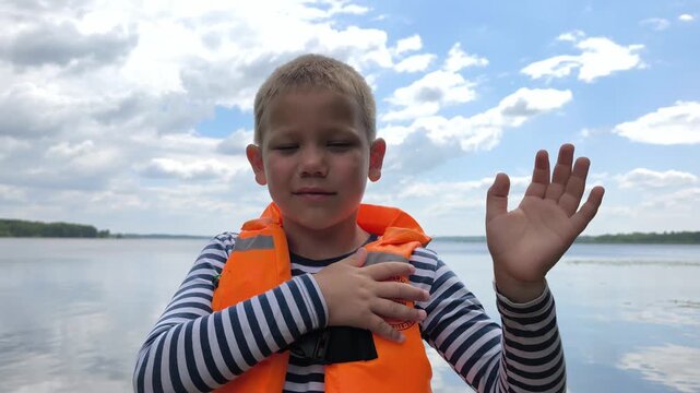 A toddler in a bright orange life jacket stands by the calm water, highlighting essential child water safety and the peace of mind that proper gear brings to family outings near lakes and rivers.