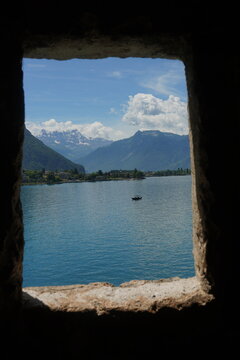 Stunning view of Lake Geneva and the snow-capped Alps framed by an old stone window inside Chillon Castle, Switzerland.
Medieval castle window framing a beautiful summer landscape of a blue lake and m