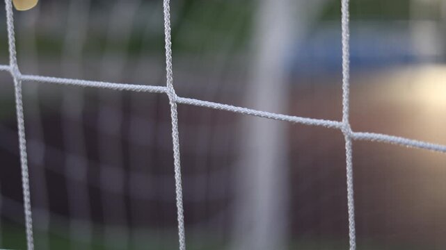 Cinematic football goal net at sunset with shallow depth of field and blurred stadium background. Professional soccer concept featuring sports, competition, teamwork, training, championship atmosphere