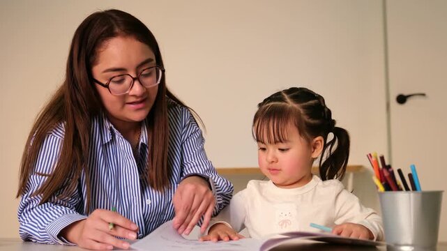 Caring female educator teaches a little girl how to draw and color during a kindergarten lesson