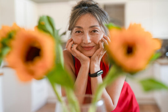 Woman smiles while resting her chin on her hands in a kitchen surrounded by orange flowers