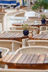 Obraz premium Cozy outdoor seating area with wooden tables, wicker chairs, and small potted plants at a hotel restaurant near a swimming pool. Elegant resort dining atmosphere with shallow depth of field
