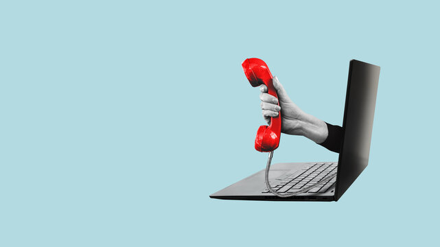 A hand holding a red landline, vintage telephone out of a laptop.