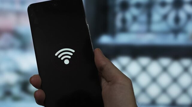 Close-up of hands holding a mobile phone showing a Wi-Fi error symbol against a rainy window background. Concept of bad internet connection and signal problems