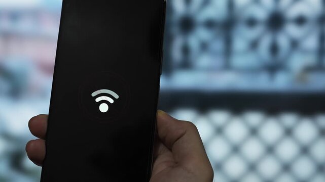 Close-up of hands holding a mobile phone showing a Wi-Fi error symbol against a rainy window background. Concept of bad internet connection and signal problems