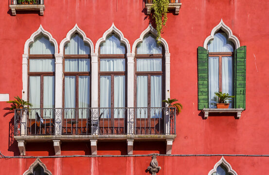 Red facade with windows and balcony of the Duodo palace in Venice, Italy