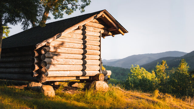 Rustic Adirondack lean-to shelter overlooking forested mountains during golden hour, surrounded by pine trees and peaceful wilderness scenery.