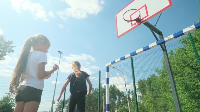 Two girls play basketball near outdoor hoop while one dribbles and teammate defends. Basketball sharpens control and timing, while basketball turns summer practice into energetic play.