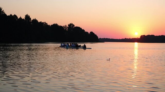 Moscow. Russia. 23.07.2026 Group of people rowing on long board in lake during golden sunset. Friends paddling on vessel on calm water. Travel and outdoor recreation adventure in nature.