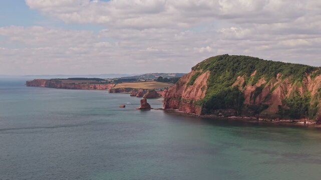 Aerial drone footage of the striking red sandstone cliffs at Jacob's Ladder Beach in Sidmouth, East Devon, England. The video captures the Jurassic Coast, dramatic coastal scenery, and the English Cha