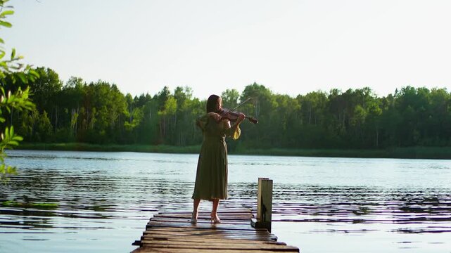 Barefoot violinist performing on a rustic wooden dock above calm lake waters, surrounded by lush green forest under clear bright summer daylight