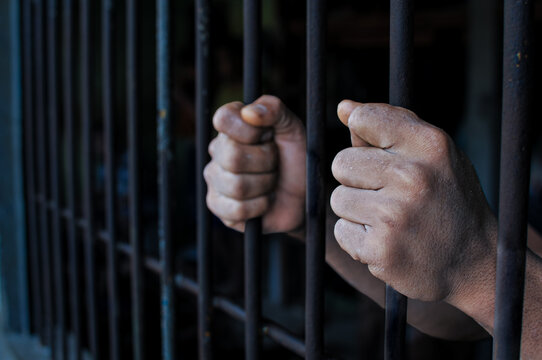 Close up of prisoner hands holding prison bars, concept of crime, justice, punishment and loss of freedom