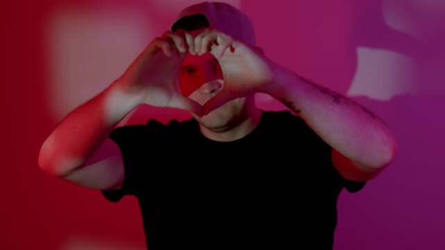 Man showing a heart gesture with his hands against a red and purple studio background. Conceptual display of love, affection and appreciation for valentine day.