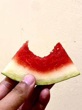 Close-up of a bitten watermelon (Citrullus lanatus) slice held by a hand. Perfect for nutrition blogs or summer food guides.