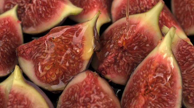 Macro shot of sweet golden honey pouring slowly over fresh cut ripe figs exposing their textured red pulp and seeds in detailed close up