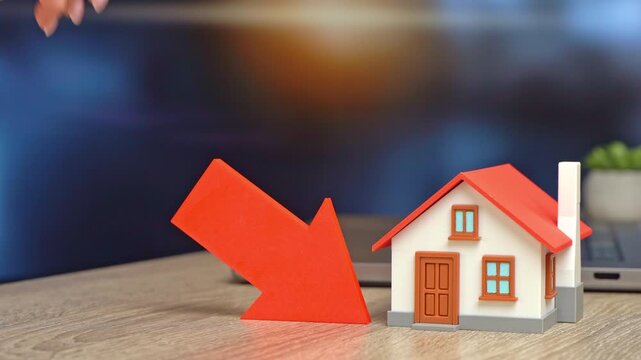 A house and a large red down arrow. Falling housing prices and declining property values in real estate market downturn and economic crisis scenario.