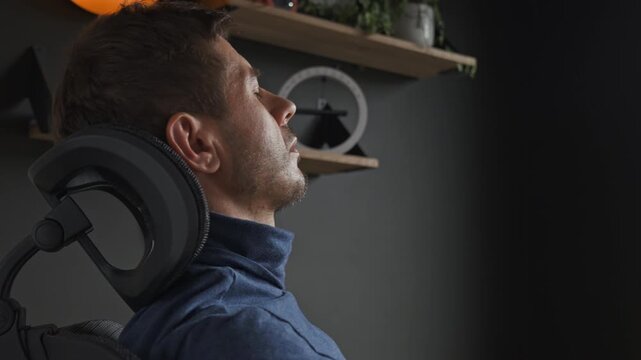 Man adjusts the headrest of an ergonomic office chair while seated at a desk, setting its position for better neck support during computer work.