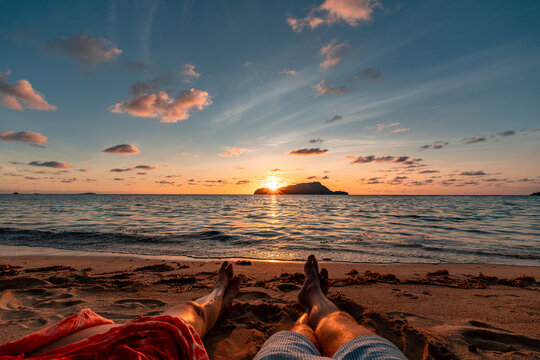 Couple relaxing on a sand beach while watching the sunset, legs visible, holiday concept