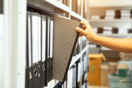 Hand of businessman office worker searching files and paperwork in the archive or document archiving storage room shelf for folder binder finding or data report record or workplace photo concept.