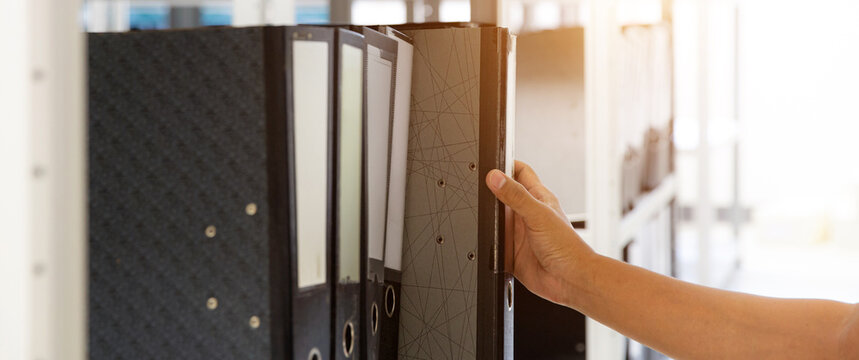 Hand of businessman office worker searching files and paperwork in the archive or document archiving storage room shelf for folder binder finding or data report record or workplace photo concept.