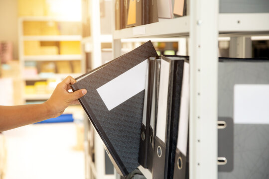 Hand of businessman office worker searching files and paperwork in the archive or document archiving storage room shelf for folder binder finding or data report record or workplace photo concept.