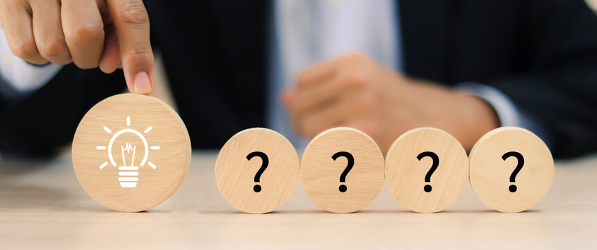 Close-up businessman hand highlighting the solution (lightbulb) on a sequence of question marks. Concept of problem solving or key of success