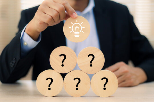 Close-up businessman hand highlighting the solution (lightbulb) on a sequence of question marks. Concept of problem solving or key of success
