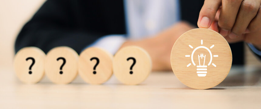 Close-up businessman hand highlighting the solution (lightbulb) on a sequence of question marks. Concept of problem solving or key of success