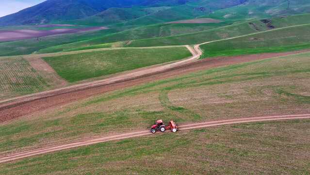 Aerial View of Red Tractor Driving Across Vast Green Agricultural Fields