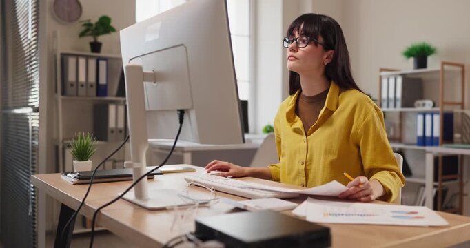 Woman accountant analyst in office using computer. She handles paperwork and finance, planning budgets and preparing tax documents for business consultation. Theme is finance and accounting.