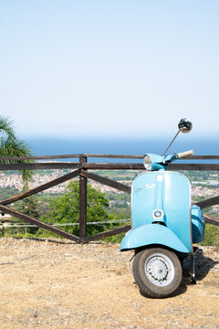 Giarre, Italy - 12 July 2026: light blue classic retro Vespa 150 Super parked by a woodem fence overlooking an Italian coastal town by the Mediterranean sea