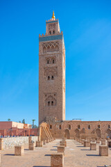 Obraz premium Kutubiyya Mosque stands tall against a clear blue sky in Marrakesh. Visitors walk in the area, taking in the structure and its surroundings during the day.