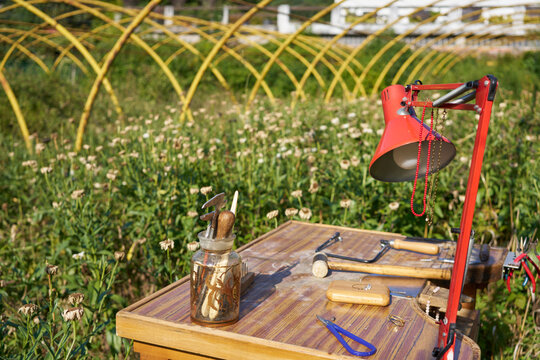 Mesa de trabajo de joyer&iacute;a artesanal con herramientas y l&aacute;mpara roja en un taller al aire libre en un jard&iacute;n