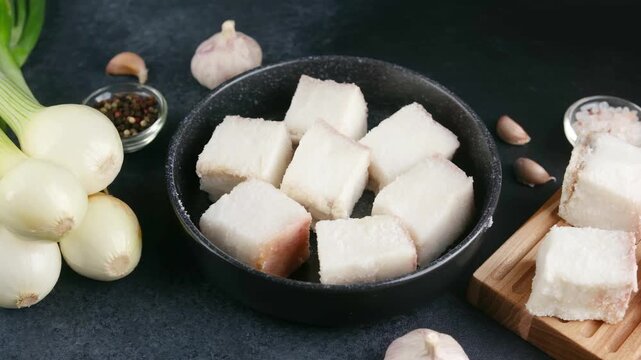 Cubes of pork fat with onions and garlic on a dark background